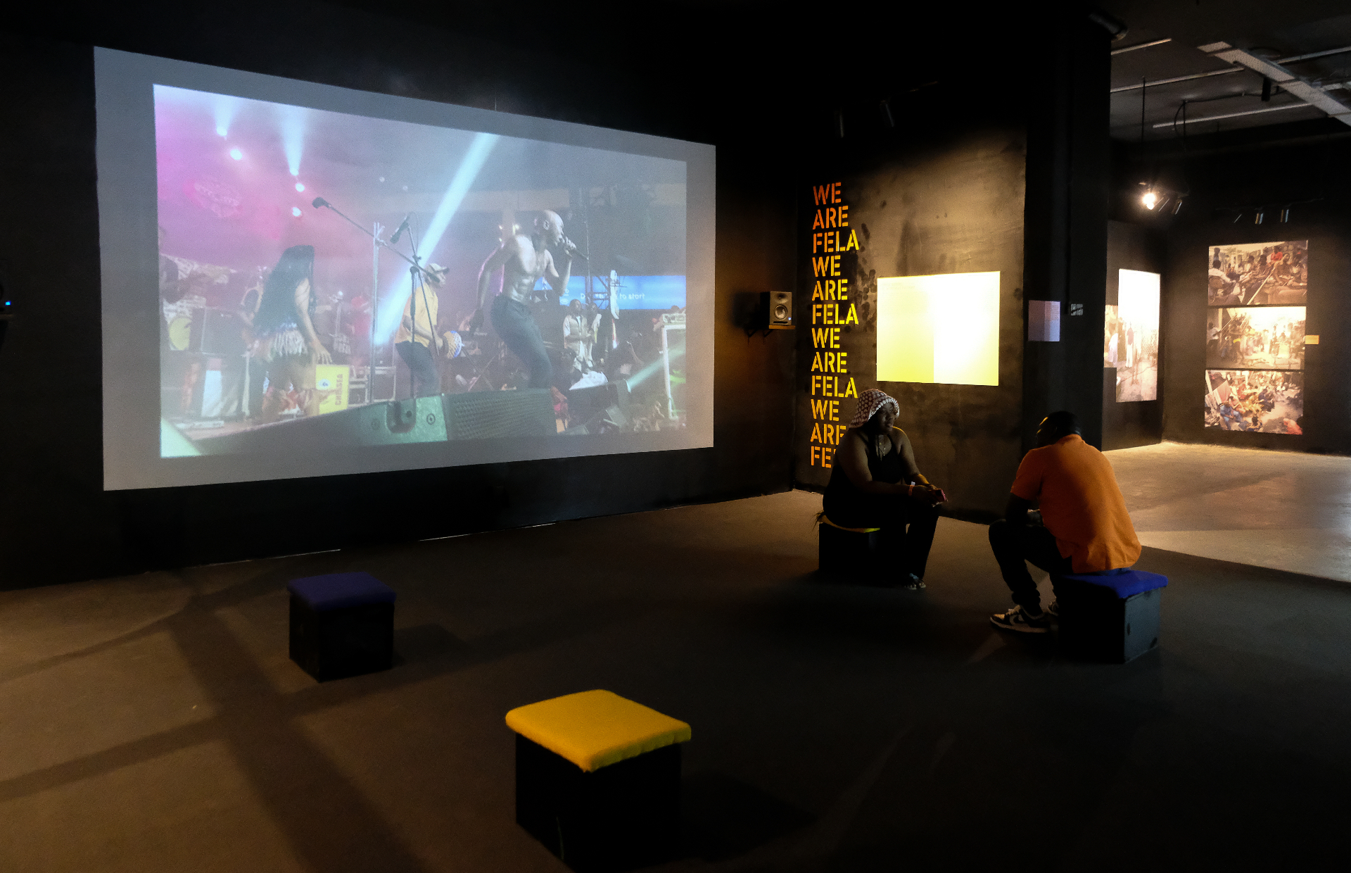 Visitors seated inside the Afrobeat Rebellion gallery facing a large performance screening beside the We Are Fela wall