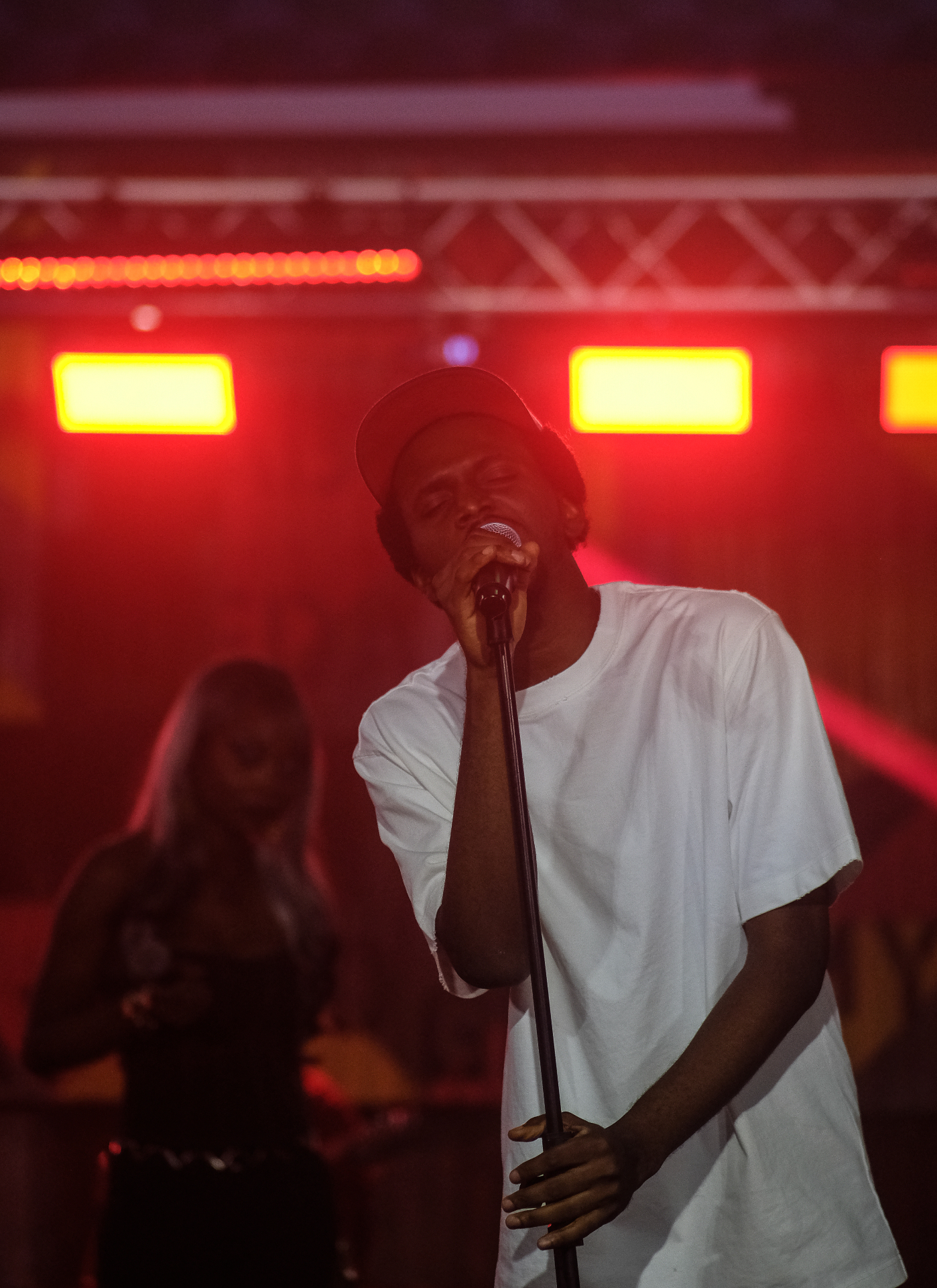Close-up of a singer in a white shirt leaning into the microphone under red stage lights at Afrobeat Rebellion
