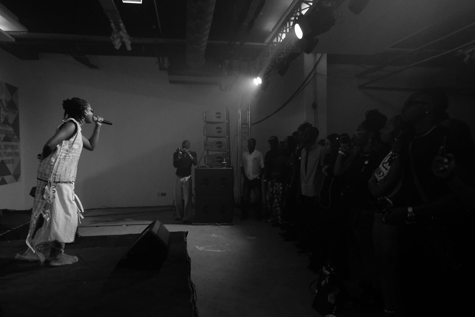 Black-and-white photograph of a singer performing to a crowd lined along the stage edge at Afrobeat Rebellion