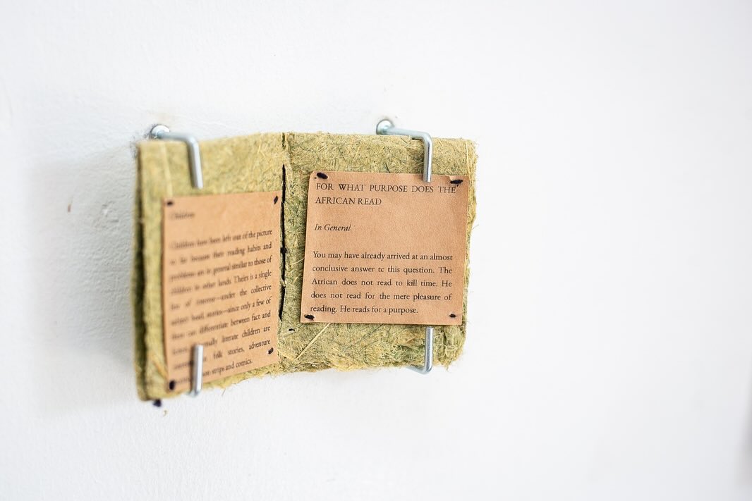 Wall-mounted plant-fibre book with printed text pages responding to the question 'For What Purpose Does the African Read'