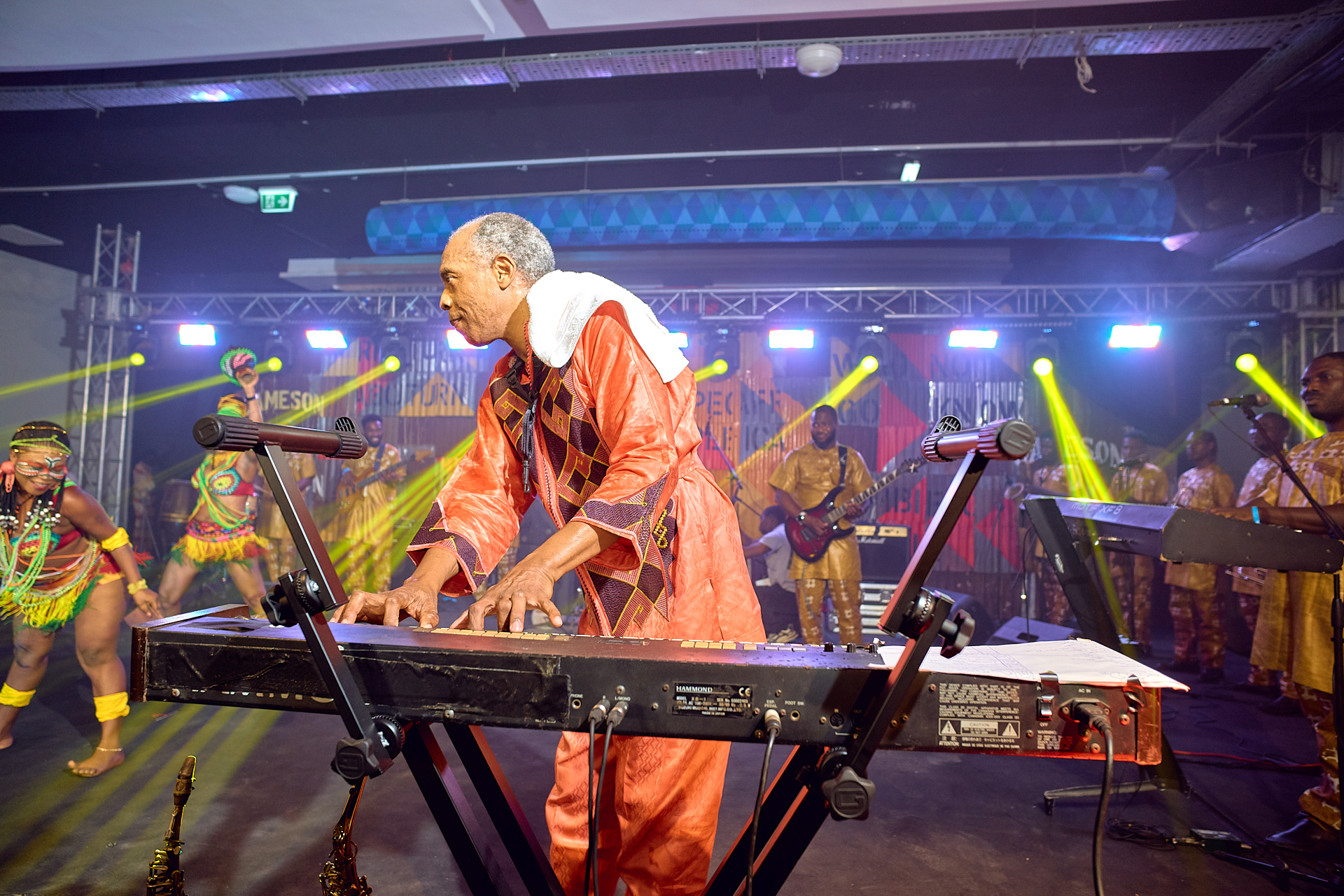 Femi Kuti playing keyboard with dancers and band behind him on stage