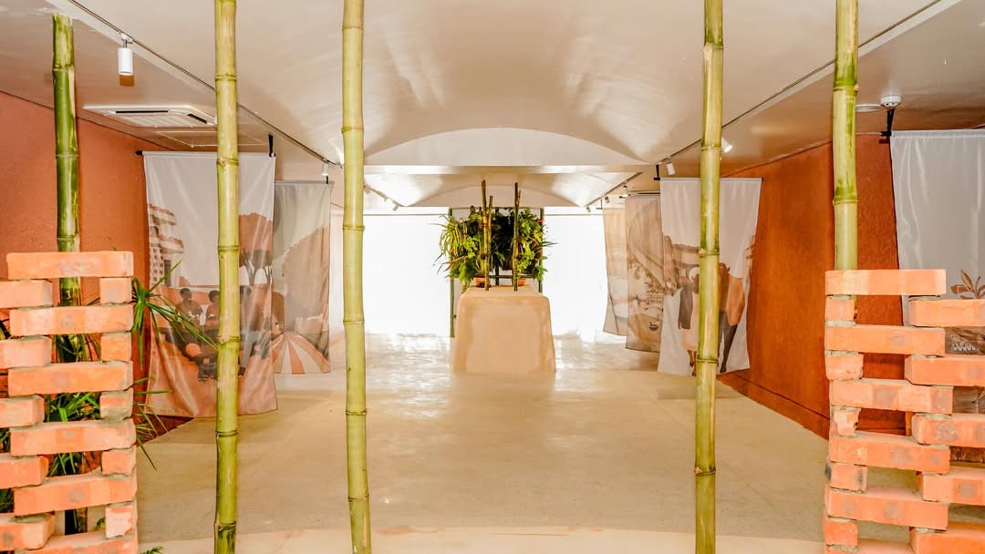Long view down the MatriAér Lab installation with textile banners, bamboo columns and a central plant altar at CCA Lagos