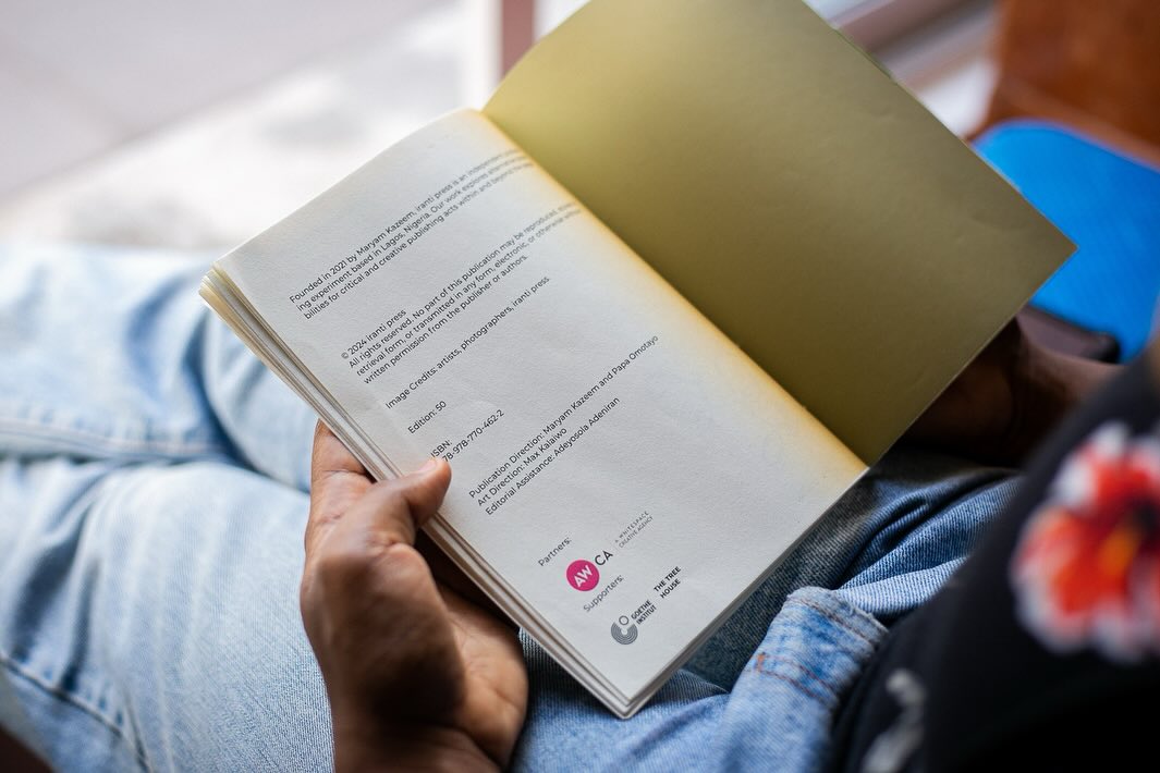 A reader holding an open publication showing the iranti press colophon and credits page