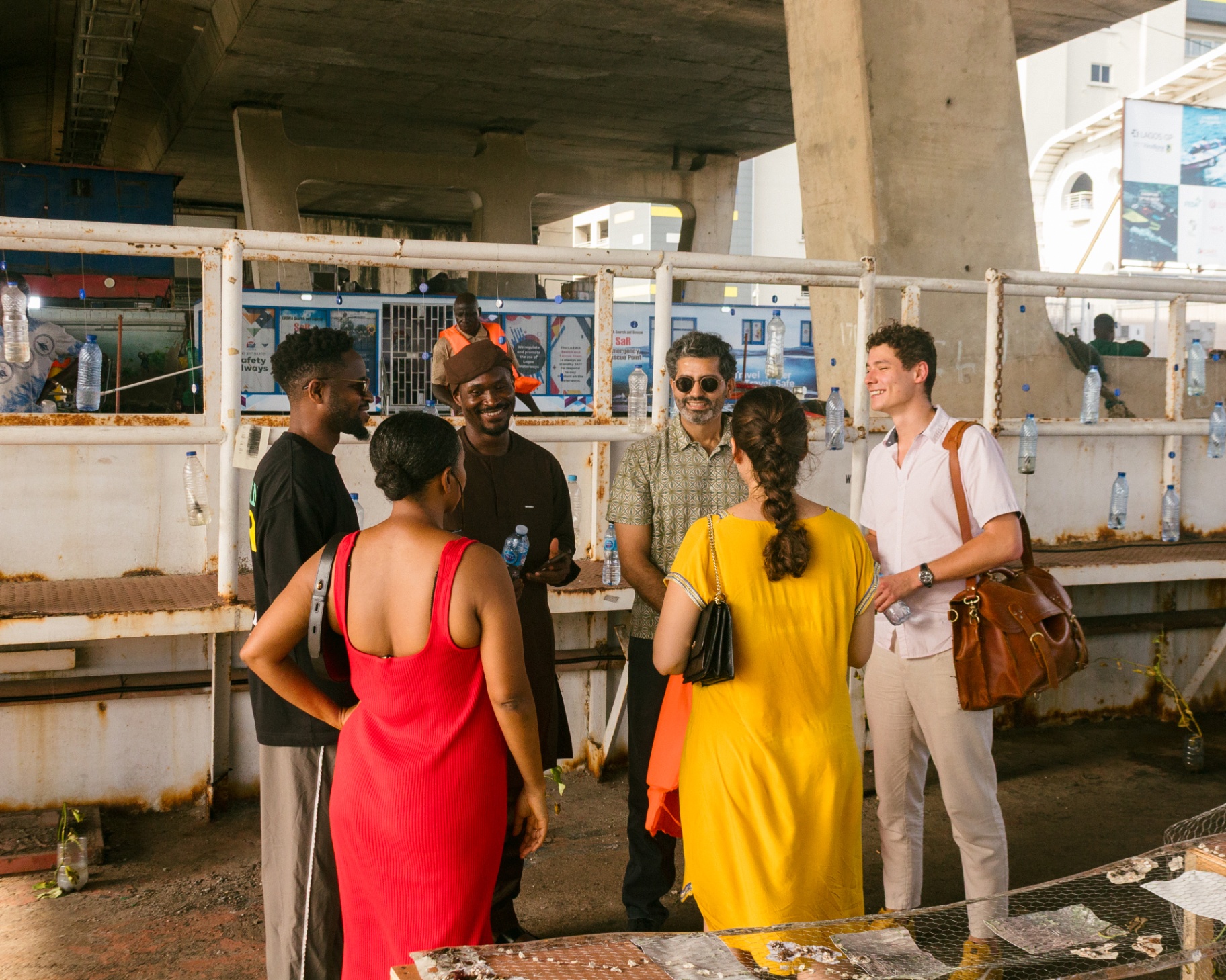 Visitors in conversation on the terminal deck, life jackets and water bottles hanging along the rusted railing behind them