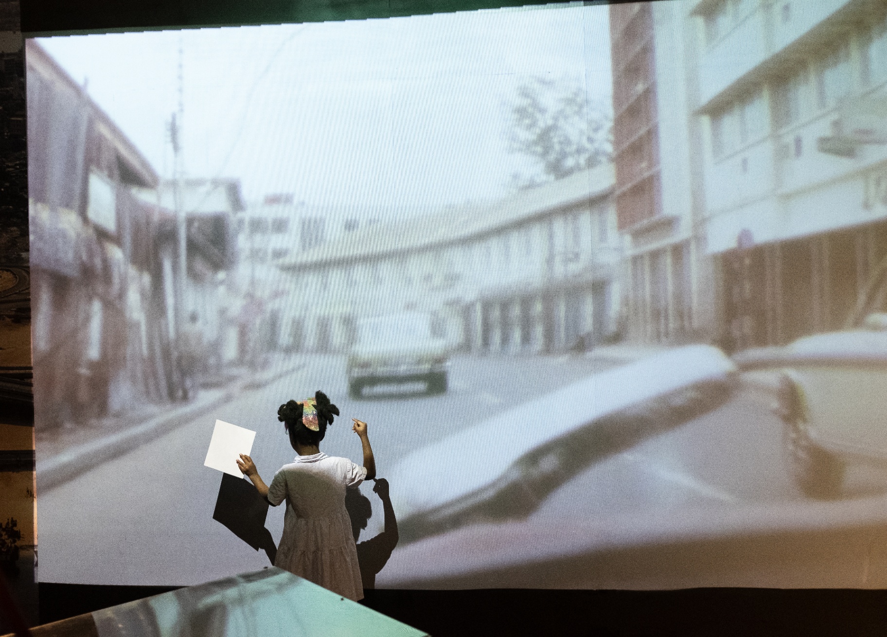 Young visitor pointing at a large projected archival street scene of Lagos inside the Afrobeat Rebellion exhibition