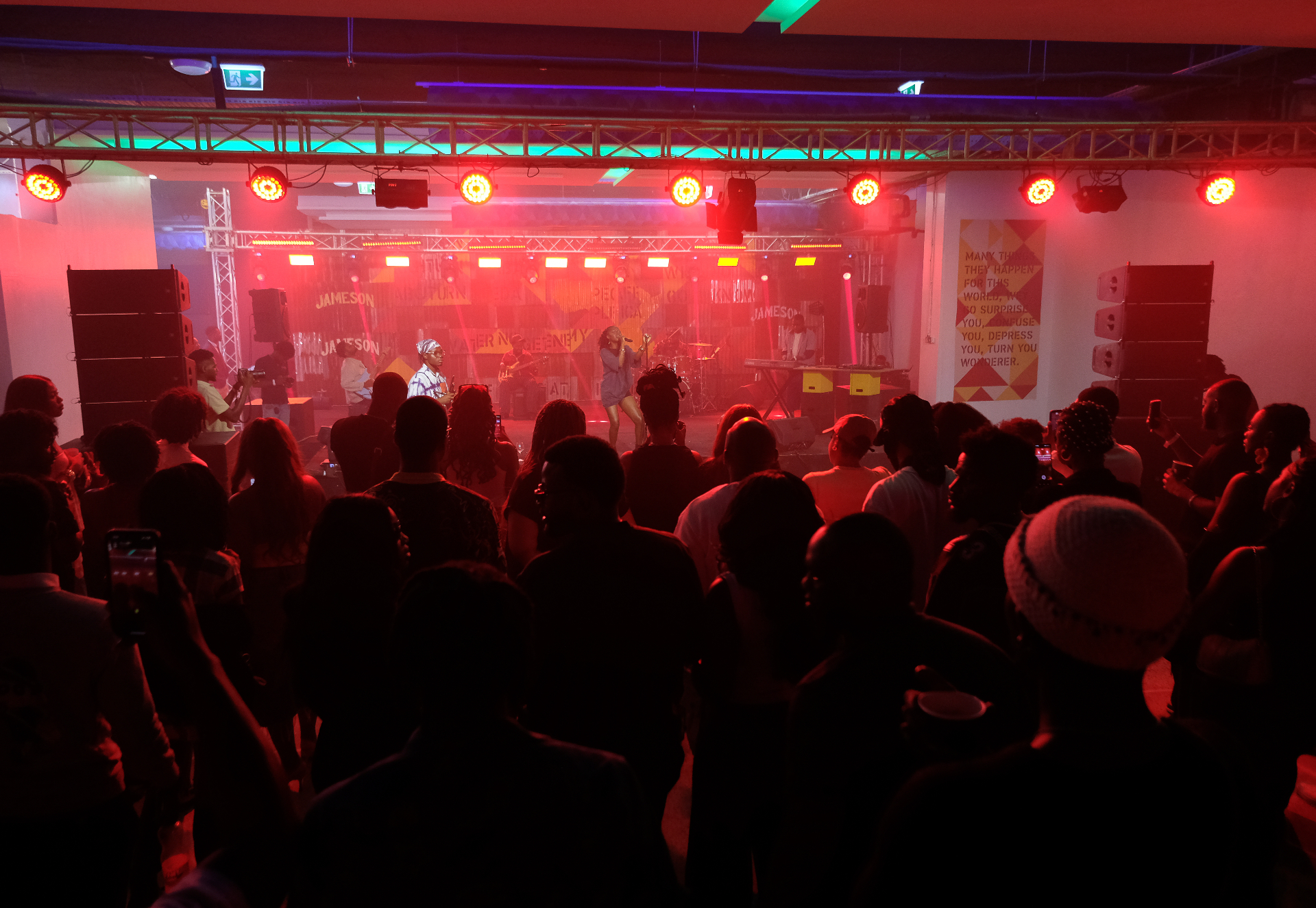 Wide view of a packed crowd facing the stage under red lights during the Afrobeat Rebellion concert