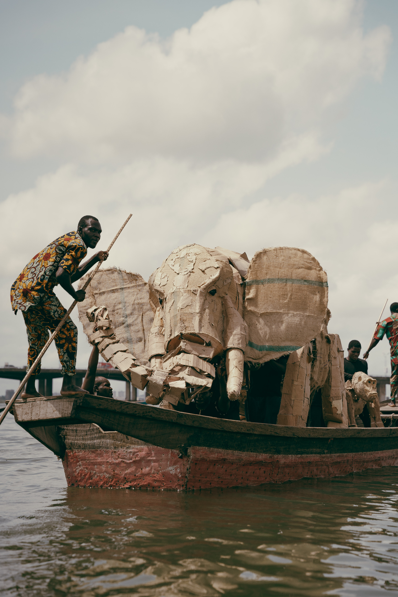 Cardboard elephant sculpture crossing the lagoon on a wooden boat