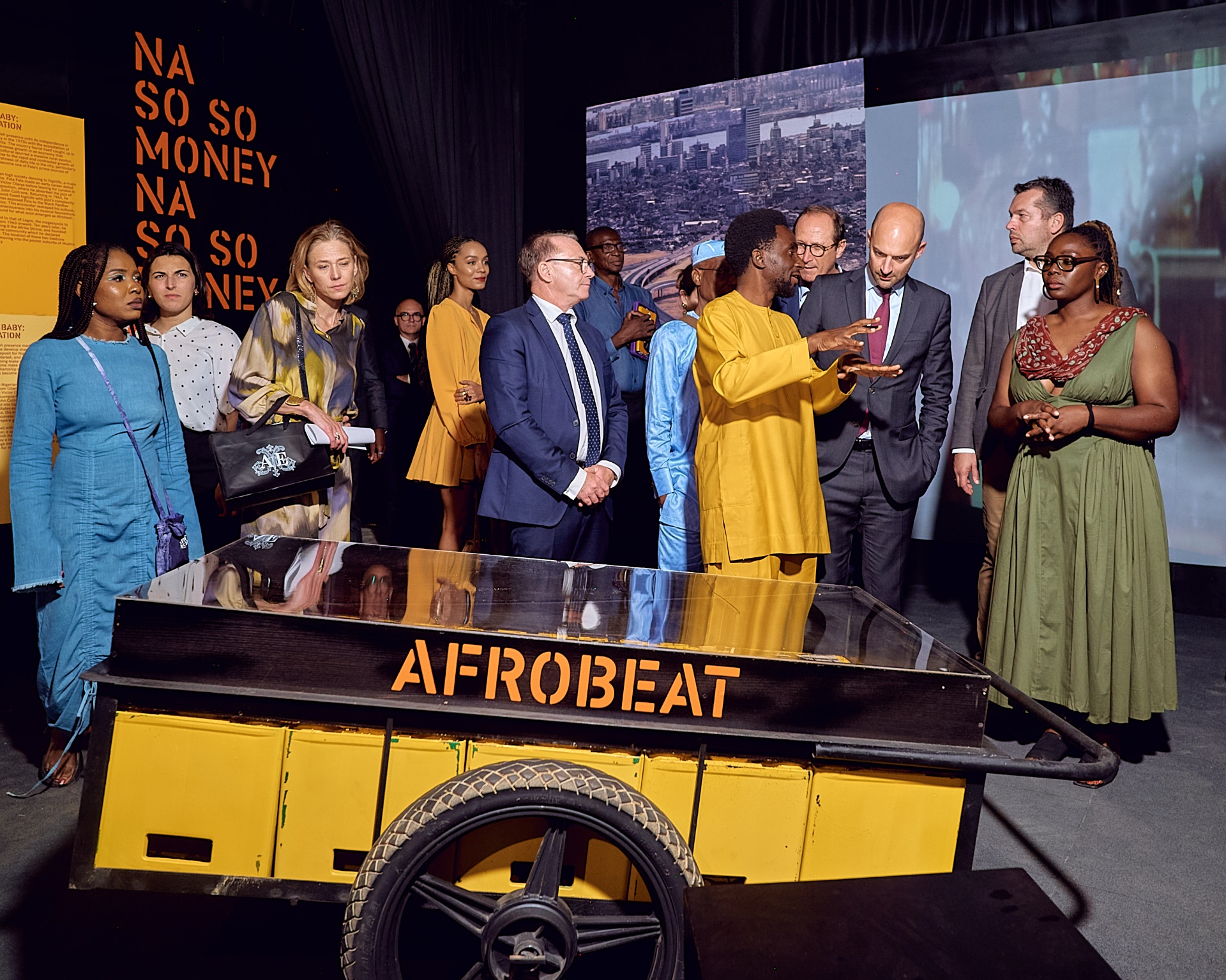 Curator addressing guests beside the yellow Afrobeat pushcart installation