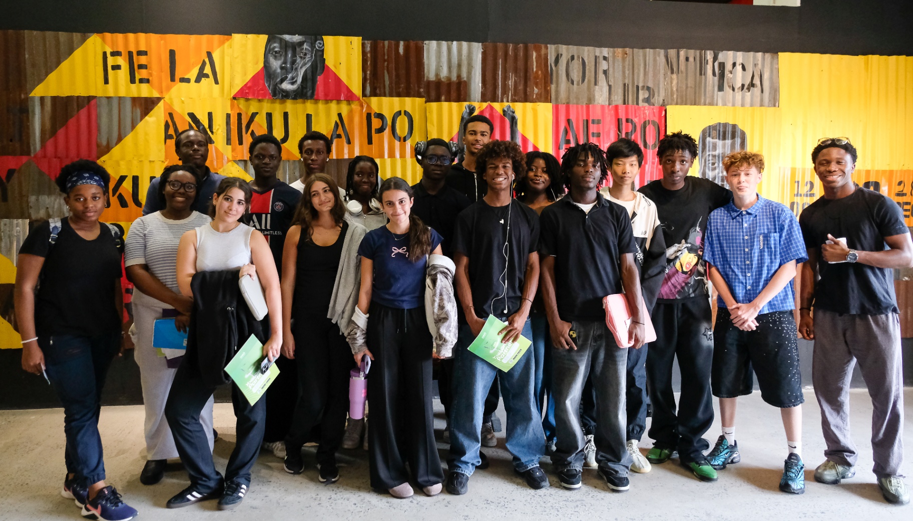 Youth programme visitors posing in front of the corrugated-metal Fela Anikulapo-Kuti mural at Afrobeat Rebellion