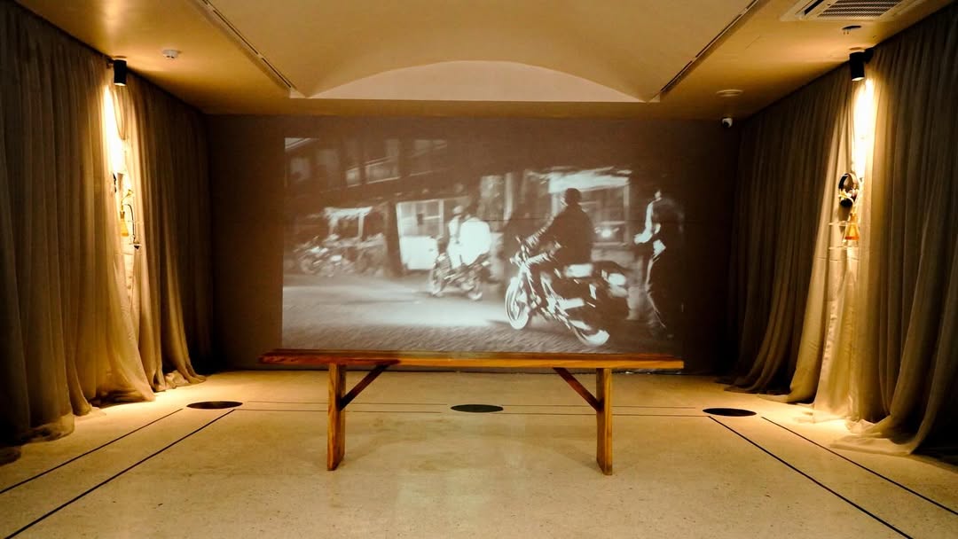 Sarauniya Ènè installation, projected black-and-white archival street scene of Lagos motorbikes behind draped curtains and a wooden bench