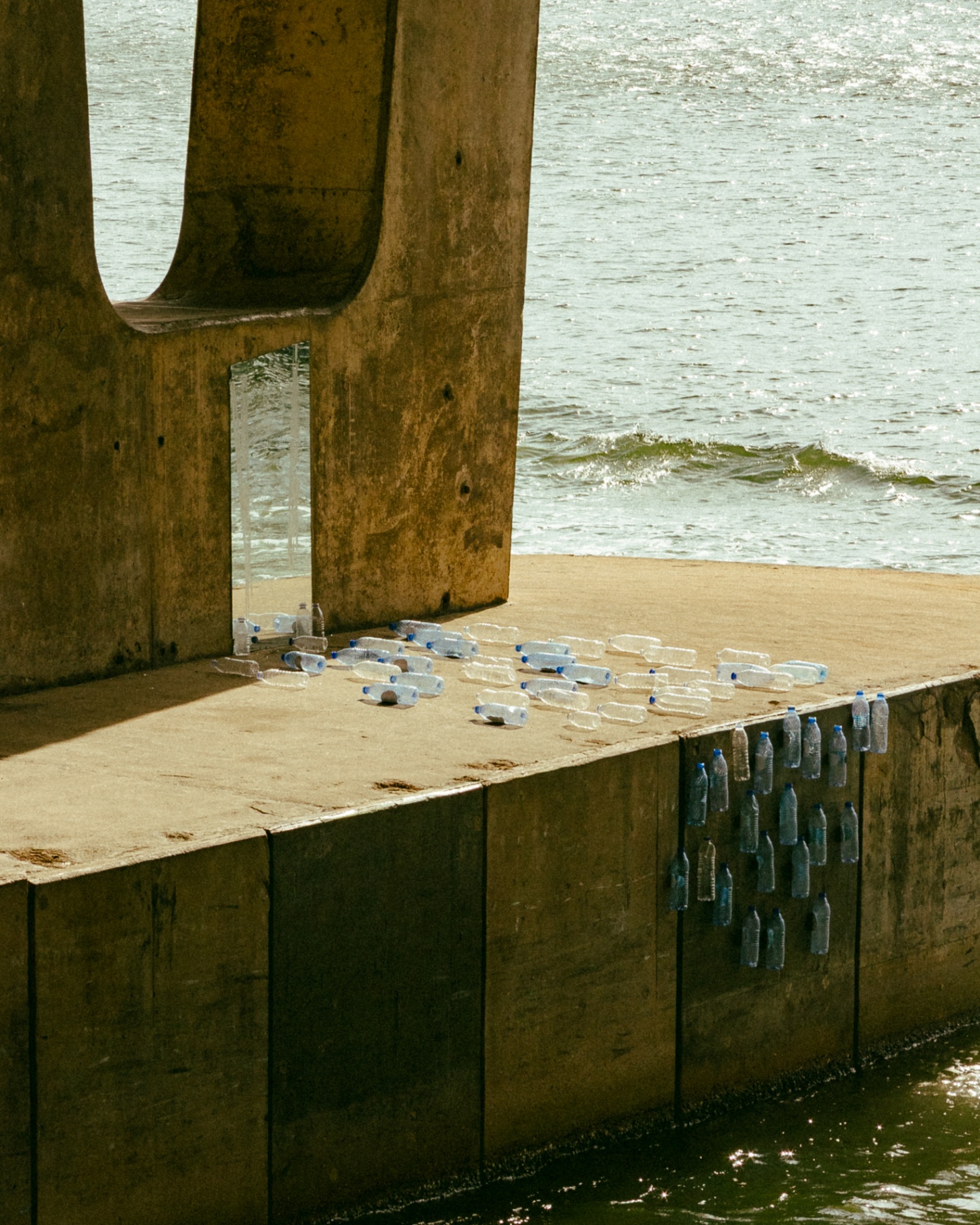 Plastic water bottles arrayed across a concrete jetty at the edge of the Lagos Lagoon, a study in accumulation and scale