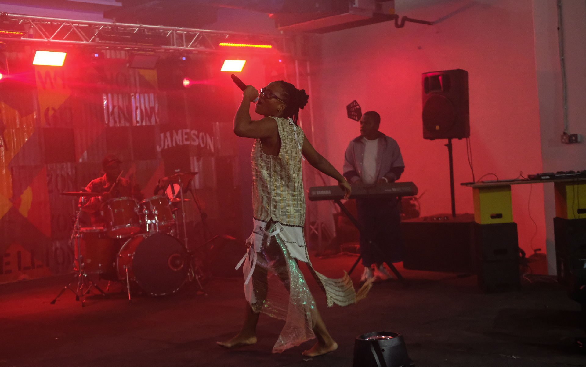 Barefoot singer performing in a sequined dress in front of the Jameson backdrop under red stage lights