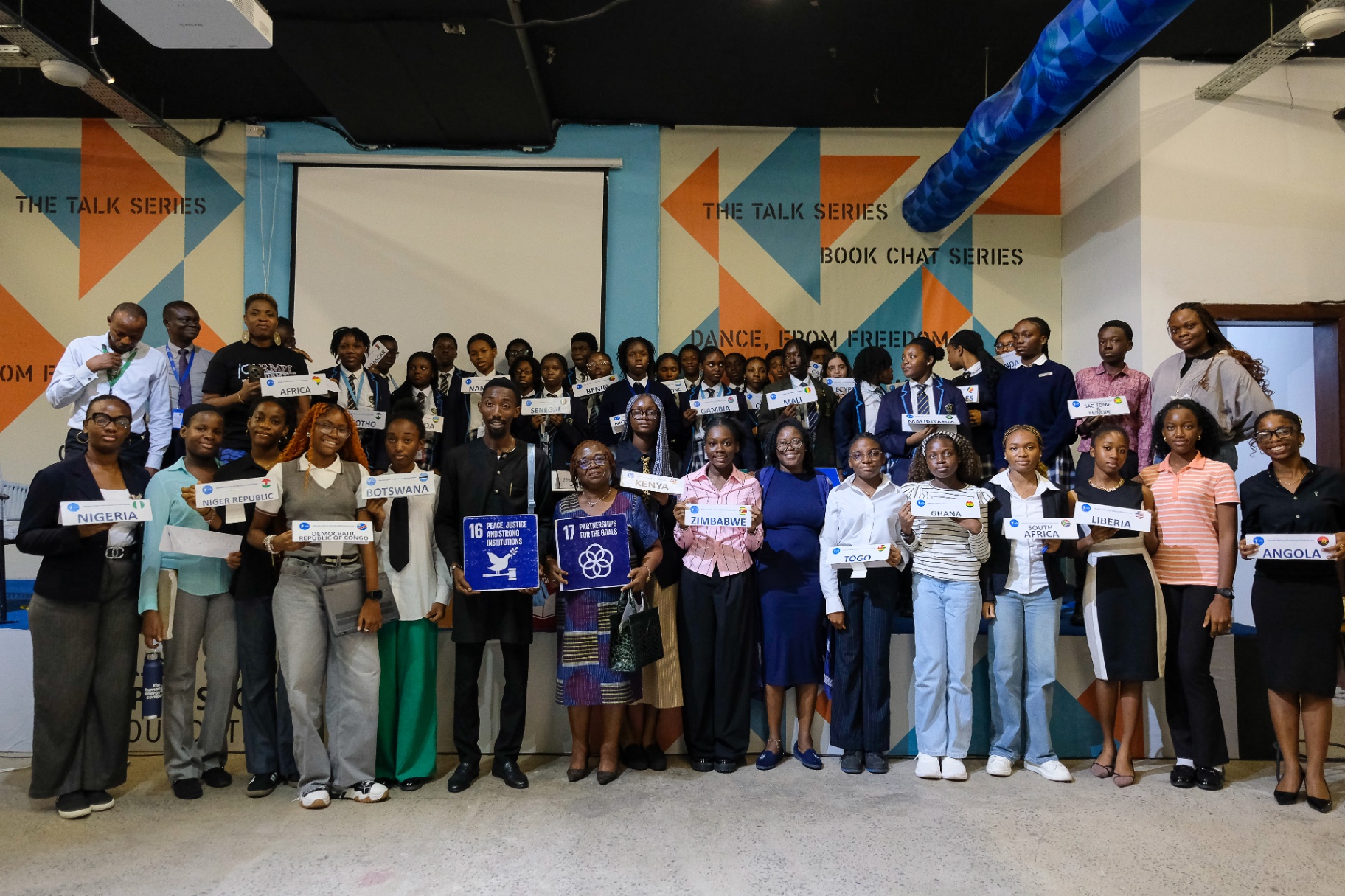 Large group of students and speakers at the Afrobeat Rebellion Talk Series and Book Chat holding country and SDG signs