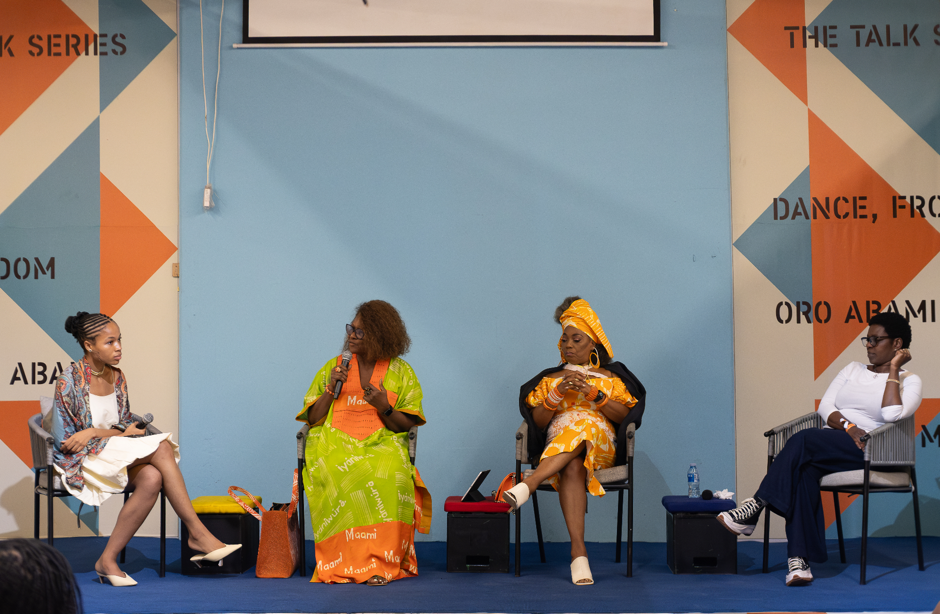 Four-woman panel on stage at the Afrobeat Rebellion Talk Series in front of the orange and blue geometric backdrop